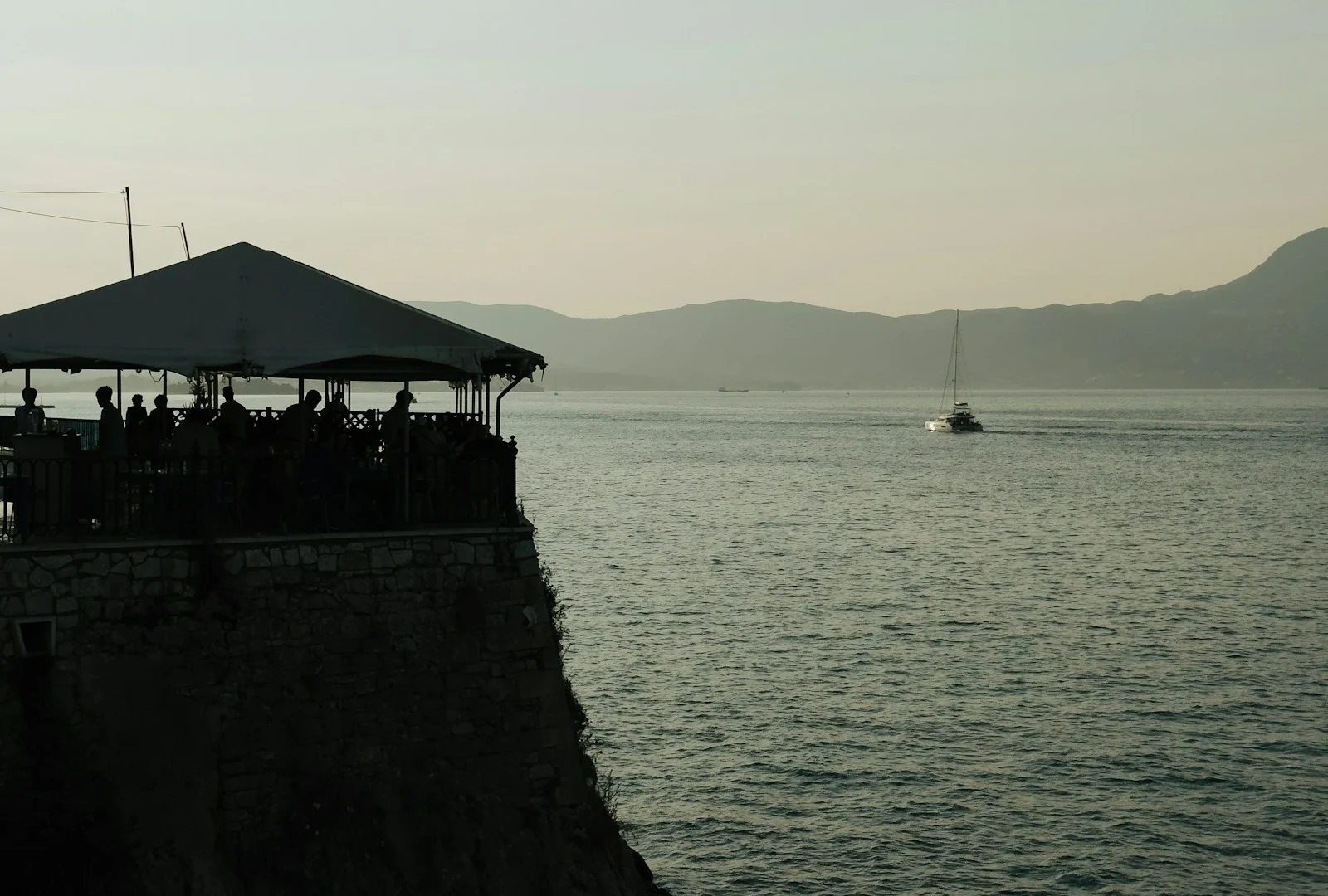 Corfu seaside terrace and distant sailboat at dusk